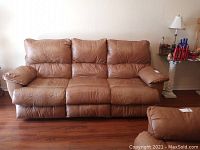 Front view of brown leatherette couch showing three seats and padded arms with worn cushions.