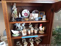 Wooden shelf displaying assorted decorative ceramic figurines including owls, rooster, and small bowls and plates