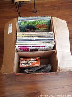 Full cardboard box filled with vinyl albums including Odilio Gonzalez and others, and a small box with headphones and bubble wrap.