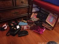 Wide shot showing assorted purses and handbags on wooden floor including black leather bags, blue purse, red sequin clutch, and beige bag with graphic design