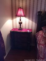 Side angle photo of wooden night stand with table lamp and patterned curtains visible