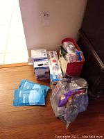 Photo of various medical supplies including face masks, bandages, and other boxed items on the floor near wall corner.
