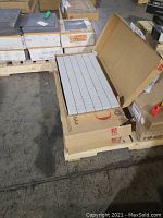 Open carton showing white ceramic mosaic tiles arranged in sheets within open cardboard box.