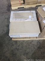 5 cartons of boxed porcelain stoneware tiles with some loose tiles on top, stacked on a pallet.