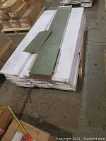 Stack of white cartons containing vinyl tiles with a couple of green tone tiles displayed on top.