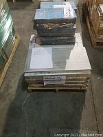 Stacked cartons of ceramic tiles on a pallet in a warehouse setting, some boxes showing minor wear, with a visible note on top.