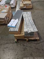Four cartons of carpet tiles stacked on a pallet with several loose tiles laid on top showing strip length and overall size.