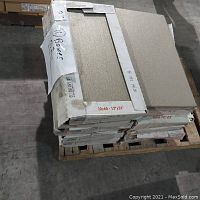 Stack of boxed tiles on a pallet with one tile displayed on top showing color and texture