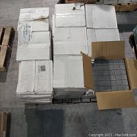 Boxes of Gallery Grey 2x2 mosaic tiles stacked on pallets in warehouse. One box open showing grey tiles in grid on sheet.
