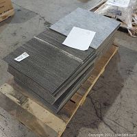 Stacked square carpet tiles in gray and white tones showing different patterns including striped and solid light gray textures.