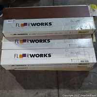 Three stacked Floorworks 6×36 brown woodgrain vinyl plank boxes with one plank sample on top