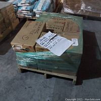 Pallet with multiple boxed ceramic wall tiles wrapped in plastic film with handwritten label on top indicating tile color and quantities.