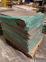 Full pallet of carpet tiles wrapped in green plastic stretch wrap on wooden skid