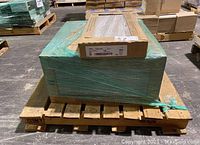Pallet of tile cases wrapped in green plastic on a wooden pallet.