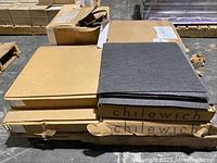 Stack of cardboard cases labeled Chilewich containing dark speckled floor tiles, with some loose tiles on top.