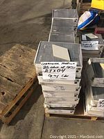 Stack of 25 boxes of Ceramiche Mutina gray tiles labeled RTEX04 with one tile resting on top showing shape and color.