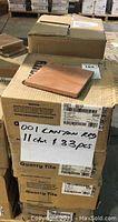 Stacked boxes labeled with Quarry Tile and code QQ01 Canyon Red, showing worn cardboard boxes and one tile displayed on top.
