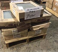 Seven unopened cardboard boxes of square porcelain tiles stacked on a pallet with a handwritten note indicating "7 boxes porcelain tiles"
