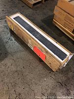 Five black slate threshold pieces packed in a wooden crate with white foam protection, showing one piece partially lifted to view thickness and finish.