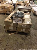 Pallet with stacked cardboard boxes and sample black river stone pebble tiles displayed on top