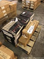 Photo showing the pallet with multiple boxes of tiles including black and brown boxes stacked and shrink-wrapped on a wooden pallet in a warehouse.