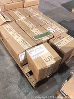 10 cardboard boxes labeled Fireclay Tile stacked on a wooden pallet in a warehouse setting. One basil green tile placed on top of the boxes for illustration.