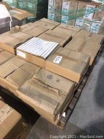 Stack of 45 boxed mosaic tiles on wooden pallet in warehouse. One box is open showing white rectangular mosaic tiles arranged in sheets.