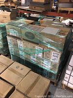 Pallet loaded with multiple stacked cardboard boxes wrapped in green plastic wrap, each box labeled and containing Marrone Canella ceramic tiles.