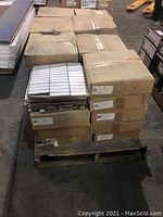 Stacked boxes of white 1x4 mosaic tile sheets on a wooden pallet in warehouse environment, visible labels indicating product type.