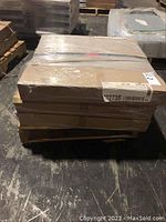 Three shrink-wrapped cardboard boxes of 24x24 carpet tiles stacked on pallets in a warehouse.