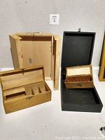 Boxes open to show interiors; smaller natural wood box has compartments, black box is empty with metal latch, tall box open showing interior space.