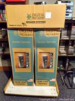 Two Digital Pro Audio speaker system boxes stacked on a cart with the top box labeled "DIGITAL PRO AUDIO SPEAKER SYSTEMS". Bottom boxes show branding as slim-line towers, made in the USA.