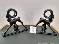 Side view of the two black ceramic ram candlestick holders on flat bases showing detailed curved horns and muscular shapes.