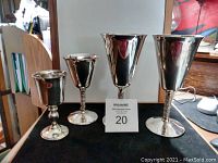Four silver plated canoeing cups on black surface, varying heights from 3 to 7 inches with twisted stems on three cups.