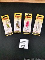 Four new Mepps spinners in original packaging, displayed on a dark surface with a MaxSold auction tag.