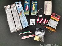 Mixed fishing tackle items on a black surface including rods, lures, hooks, and rigging accessories.