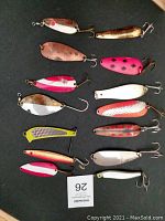 Photo displaying 14 vintage fishing lures of different colors, patterns, and shapes scattered on a dark surface.