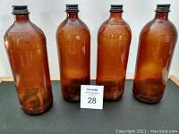 Four amber glass bottles with embossed Javex text and black screw caps, arranged in a row.