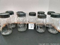 Nine vintage mason jars, six Canadian Jewel and three Crown, arranged in two rows on flat surface. All jars have metal screw-top lids showing signs of aging.