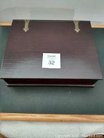 Closed wooden rectangular memory box with two brass hinges on the top side and visible screws, dark brown finish.