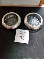 Top view of two round sterling silver coasters revealing the glass starburst inserts and beaded silver rims.