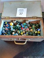 Top-down view of the open wooden box filled with an assortment of glass marbles in multiple colors and sizes.