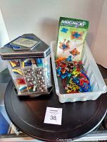 Hexagonal container filled with silver metal spheres and plastic rods, beside plastic tray holding colorful connectors and instruction booklet