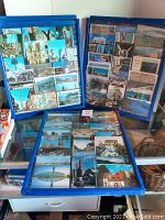 Three blue vintage postcard display cases filled with assorted postcards, shown arranged on a table.