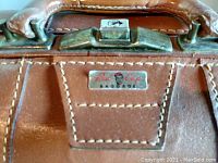 Close-up of metal latch and Red Cap brand metal plaque on leather surface