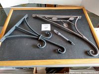 Three different wall mounting plant hangers laid on a black surface, including a bracket with leaf design and two with scroll work.