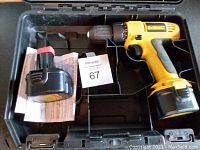 Opened case showing yellow and black cordless driver/drill with adjustable clutch, rechargeable battery pack, and instruction manual inside.