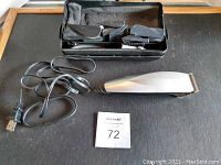 Photo showing Remington hair clipper with attached power cord and a black carrying case containing the clipper and attachments.