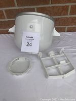 Full view of the white KitchenAid ice cream maker freezer bowl with the lid and paddle parts on a white cloth background.