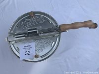 Whirley Pop popcorn maker showing top lid with embossed logo, metal construction, and wooden handle.